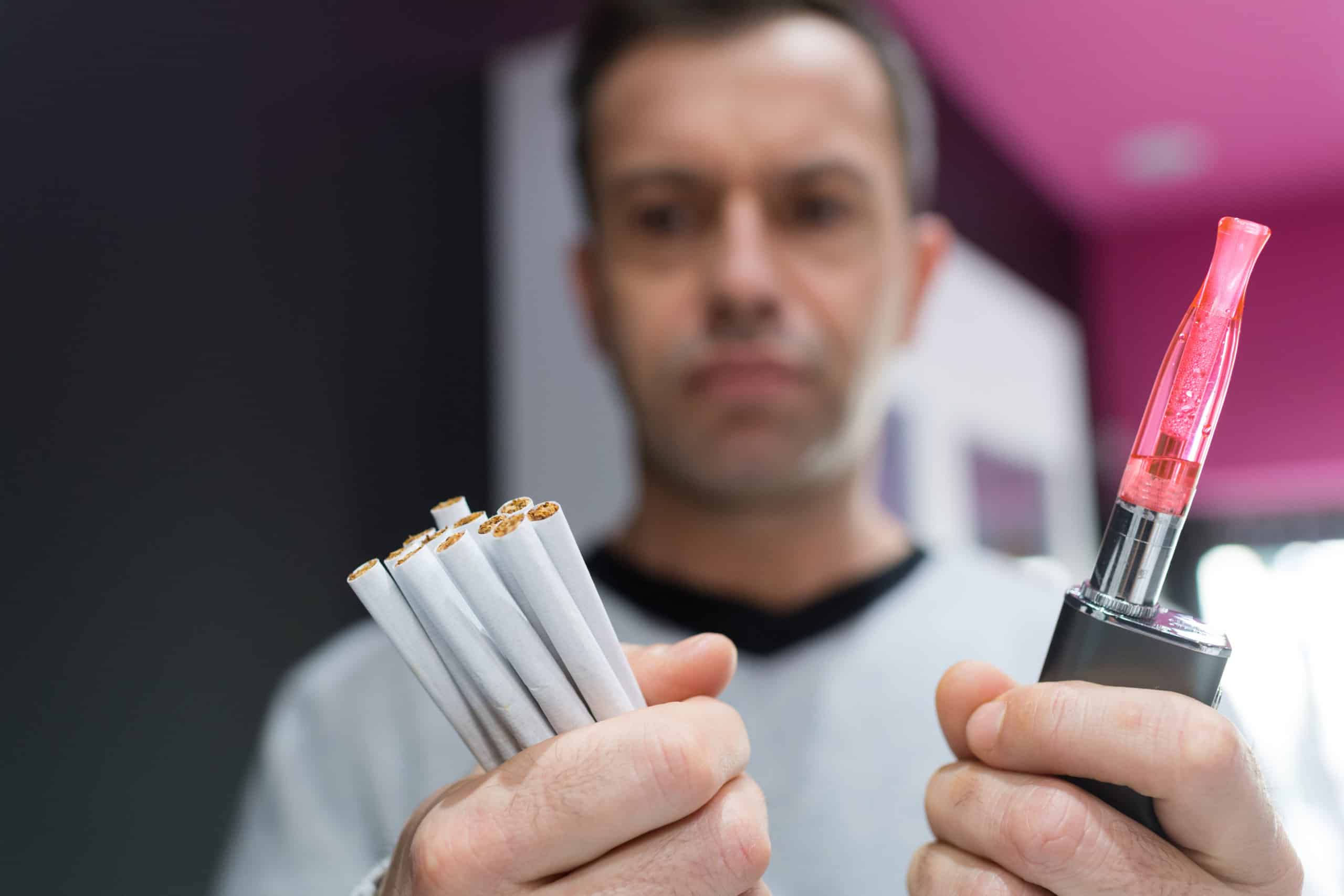 Adult man chooses between cigarettes and vape device.